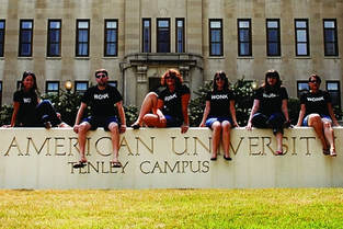 Six students sitting on a campus sign in front of a university building